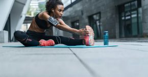 Fitness woman with earphones exercising and stretching outdoors on fitness mat