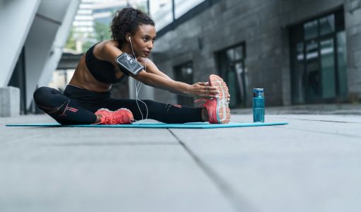 Fitness woman with earphones exercising and stretching outdoors on fitness mat